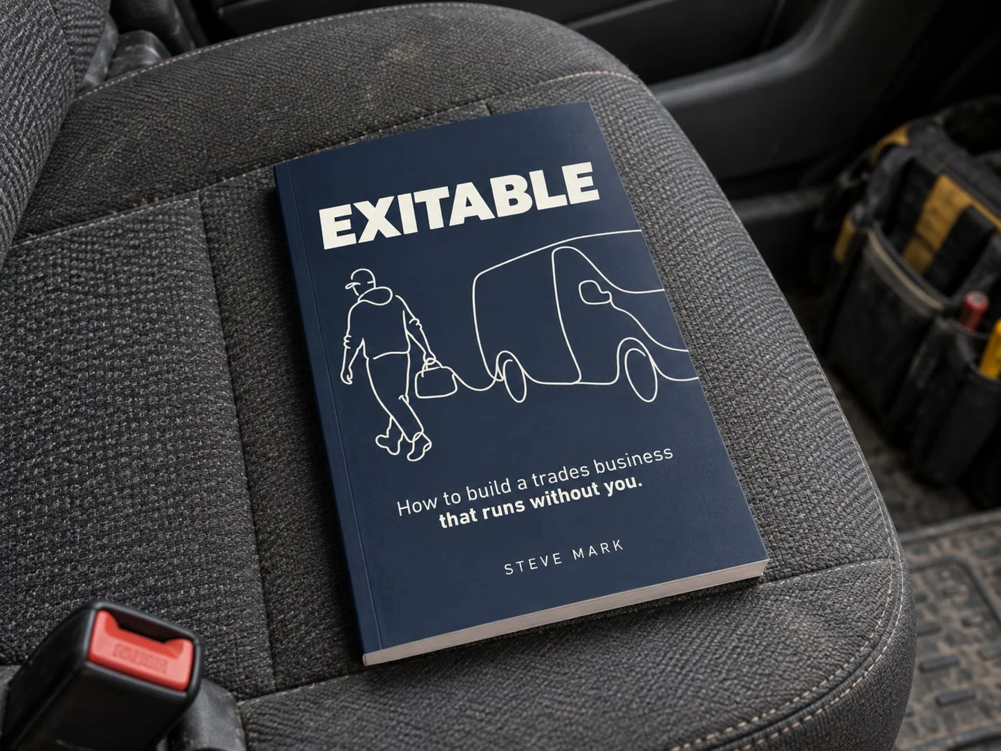 A copy of EXITABLE by Steve Mark on the passenger seat of a work van, beside a tool bag.