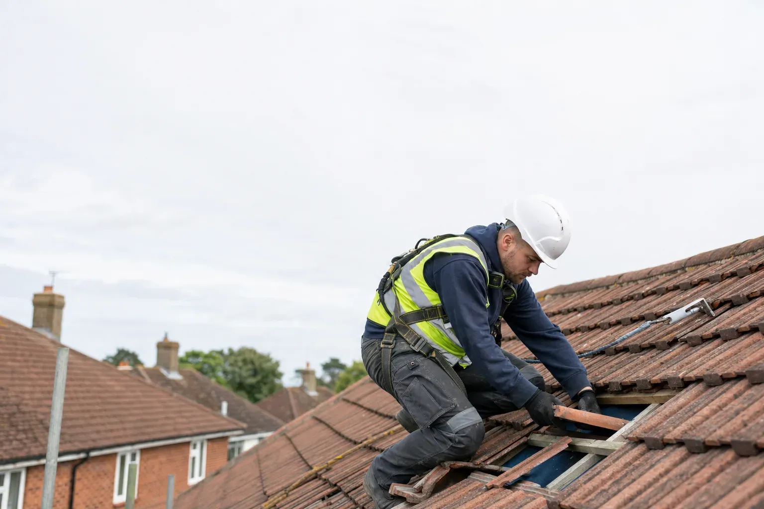 A roofer in a harness and hi-vis replacing a tile on a UK pitched roof.